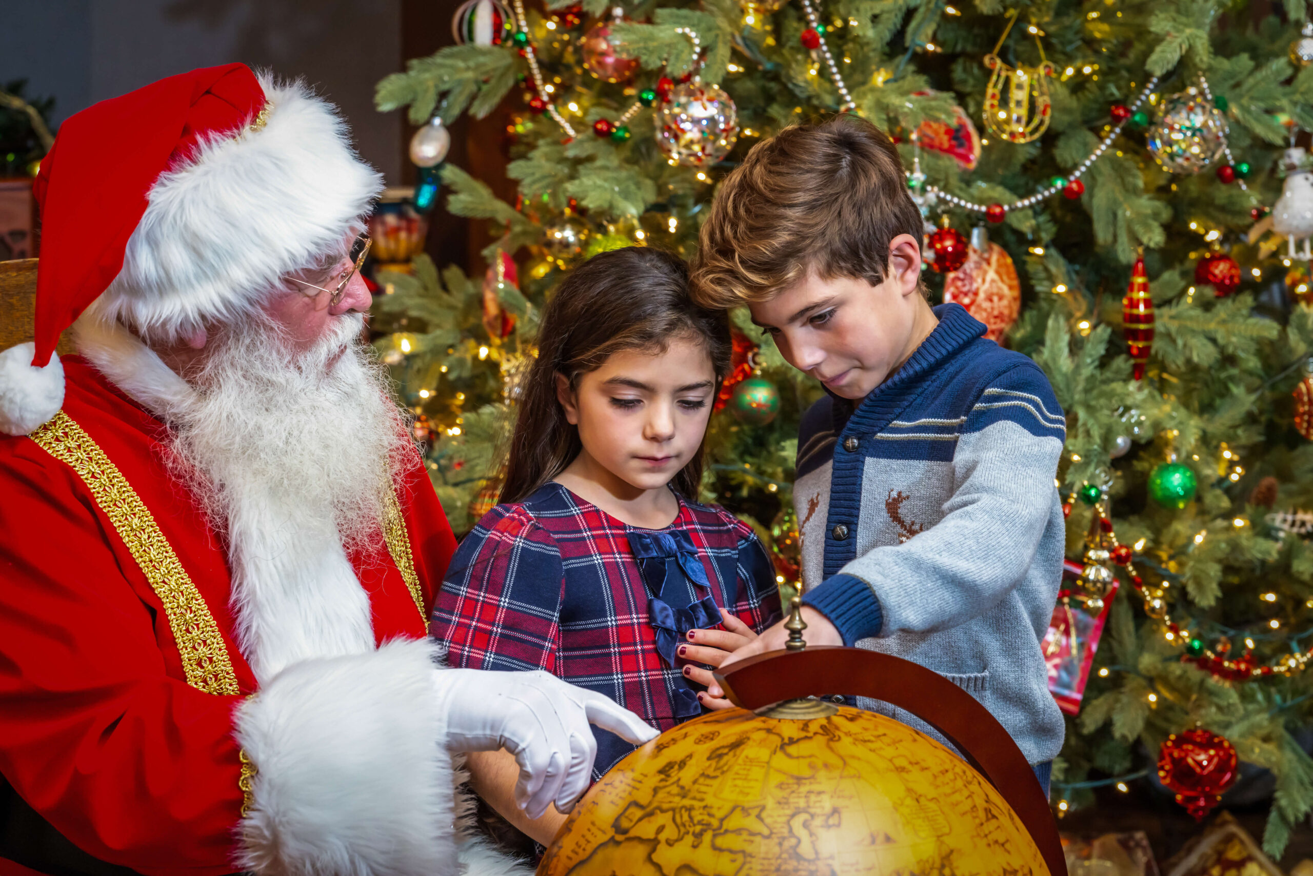 boy and a girl pointing at the globe with santa claus