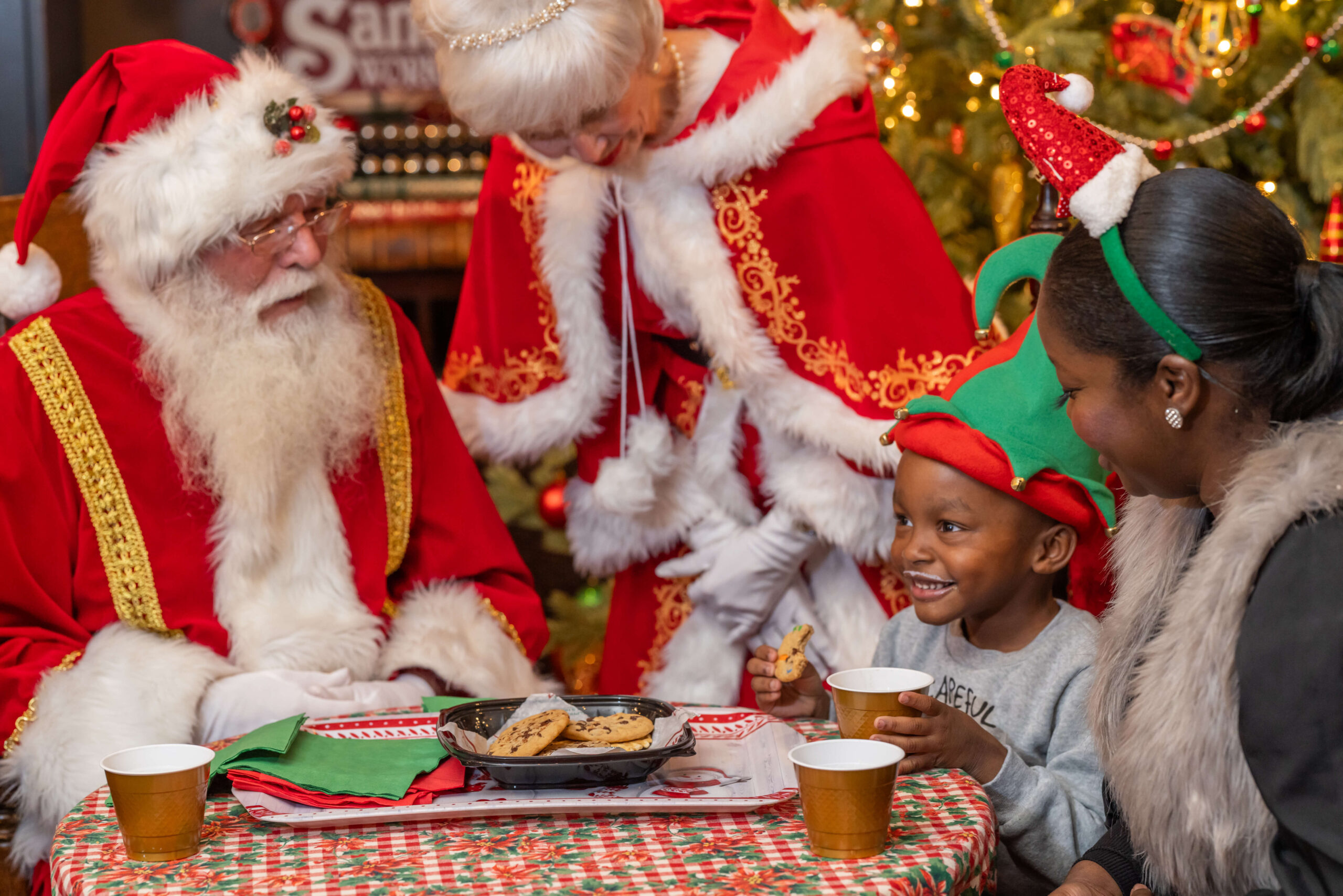 young boy with a milk mustache eating cookies with santa and mrs. claus