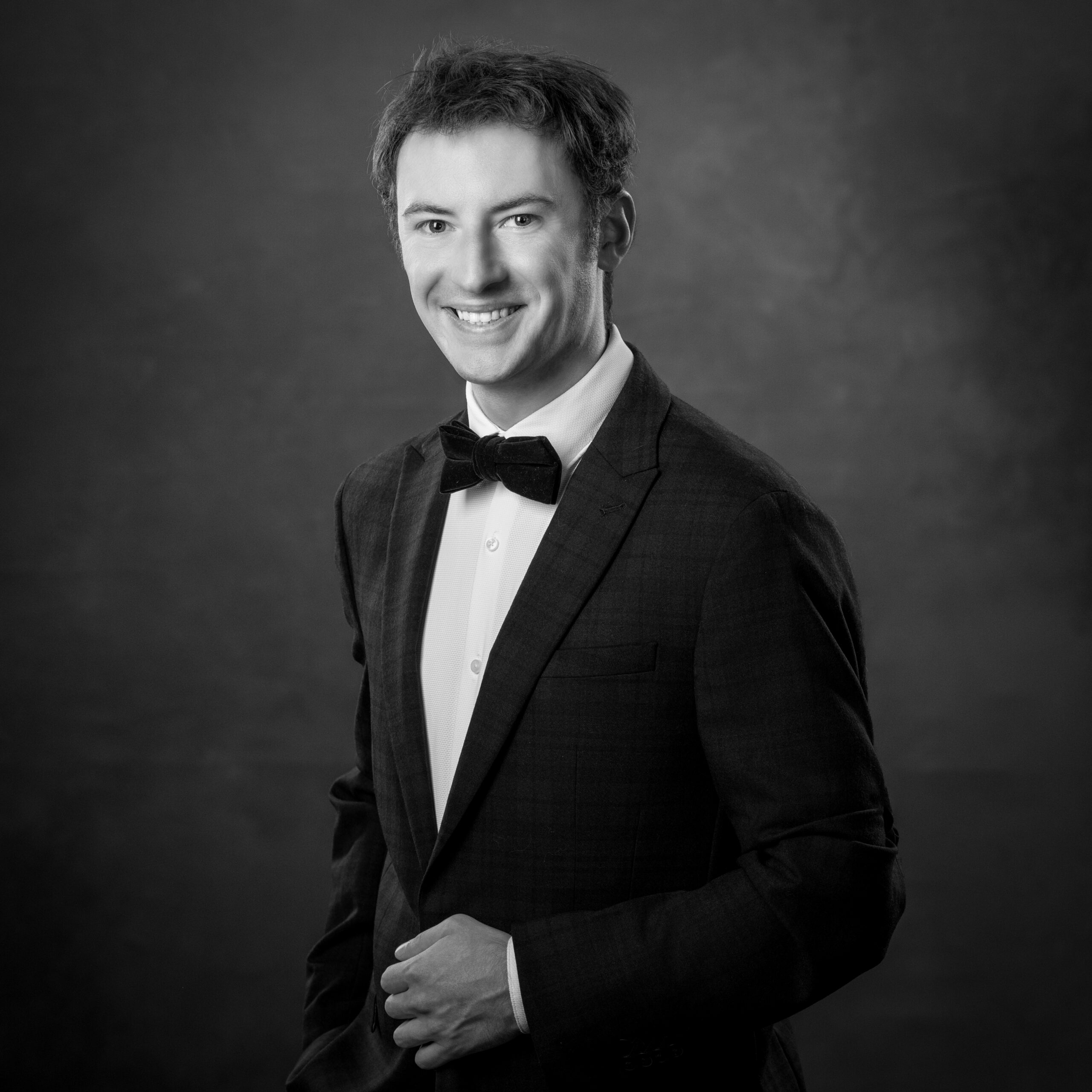 Smiling man in a suit and bow tie, hand in pocket, black and white portrait.