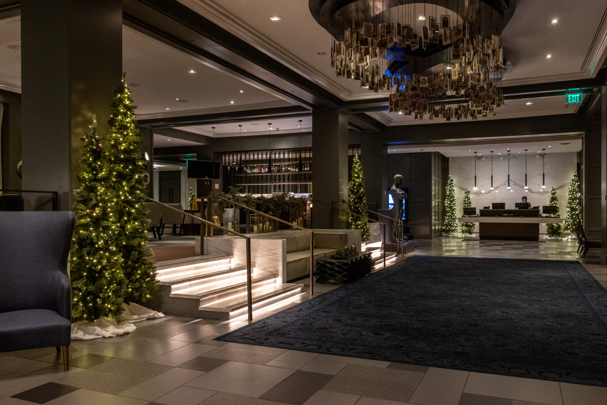 Hotel lobby with Christmas trees, elegant chandelier, and a reception desk in the background.